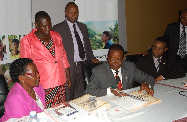 The Minister signing the Strategy. On the left: Rachel Musoke, representing the Permanent Secretary, MWE, and Members of the Parliamentarian Forum on Climate Change. On the right: H.E. Abel Rwendeire, Deputy Chair of the NPA, and Safiou Esso Ouro-Doni, UNDP Deputy Country Director.